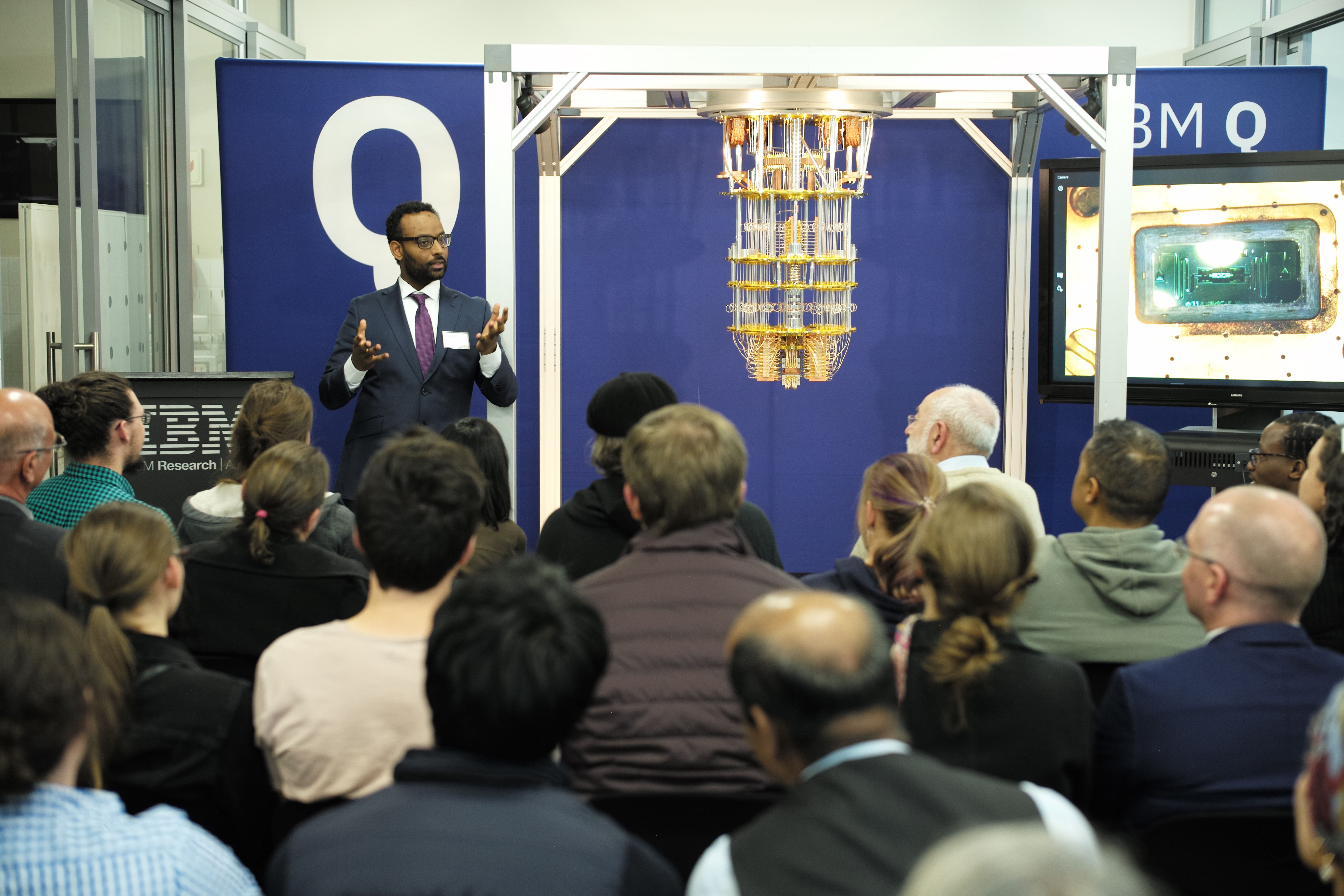 Abraham Asfaw standing in front of a quantum computer and speaking to a group of developers at the 2019 IBM and Wits University Quantum Meet-Up in Johannesburg